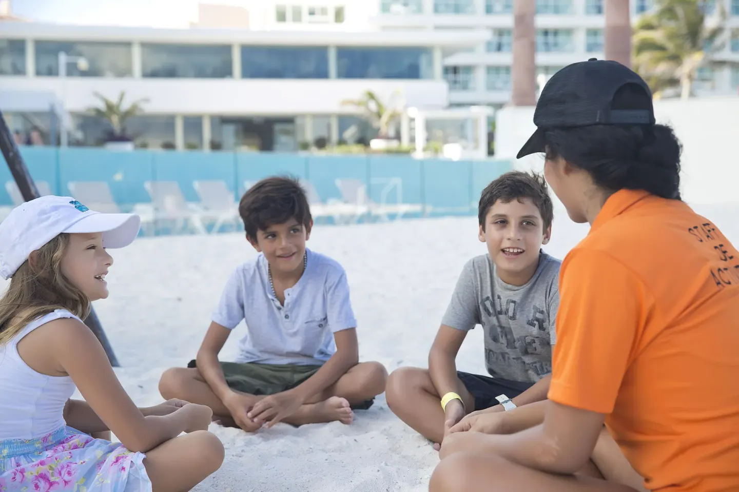 Children sitting on the sand with a resort activity staff member at Krystal Cancun.
