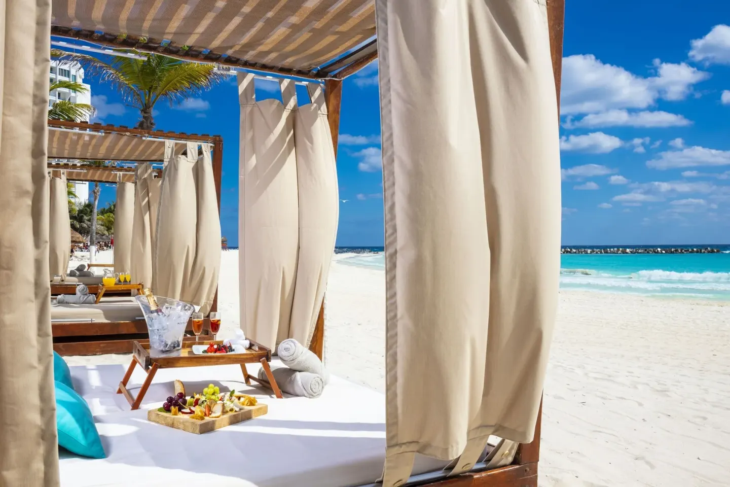 Beach cabanas with curtains, fruit trays, towels, and turquoise sea at Krystal Cancun.