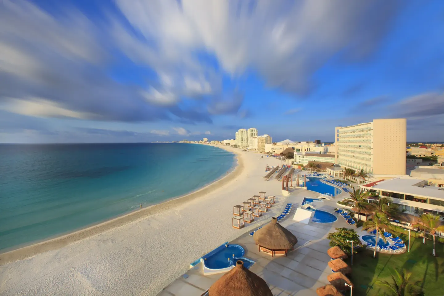 Beachfront pools and white sand shoreline at Krystal Cancun under a dramatic blue sky.