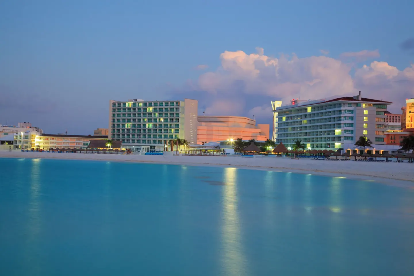 Krystal Cancun beachfront buildings glow at dusk beside calm Caribbean water.