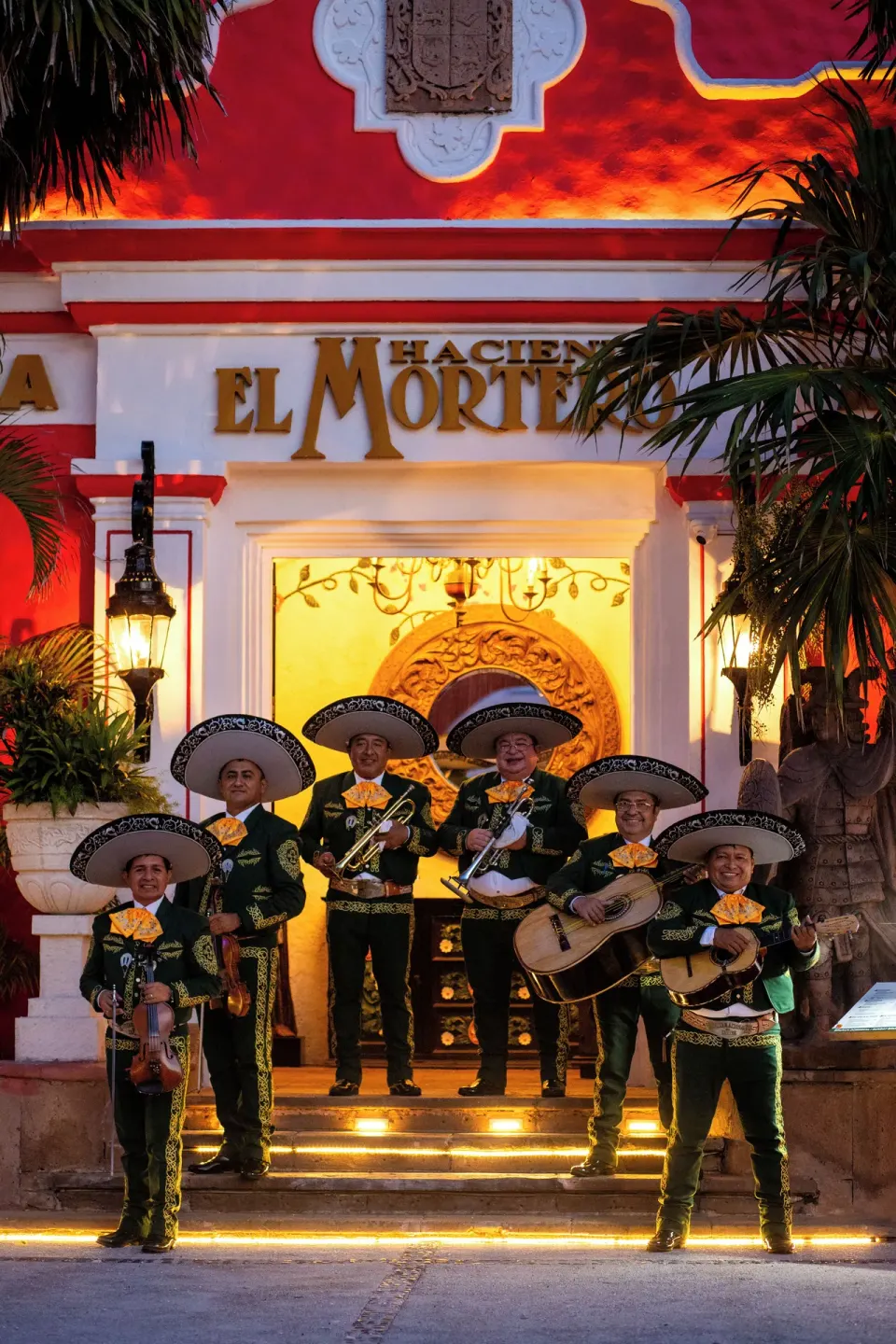 Mariachi musicians outside Hacienda El Mortero near Krystal Cancun in front of a brightly lit red facade.