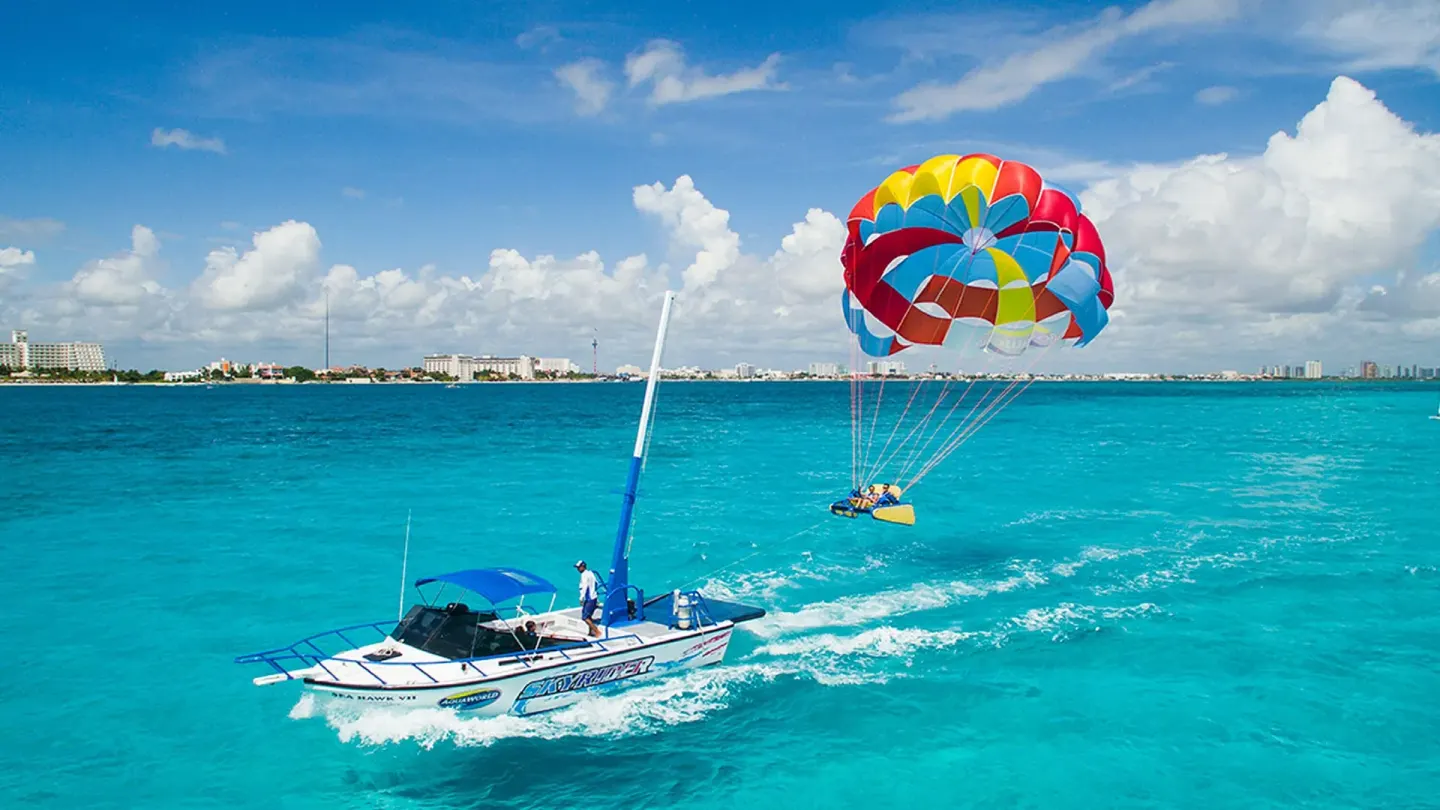 Parasailing boat towing a colorful parachute over turquoise water near Krystal Cancun.