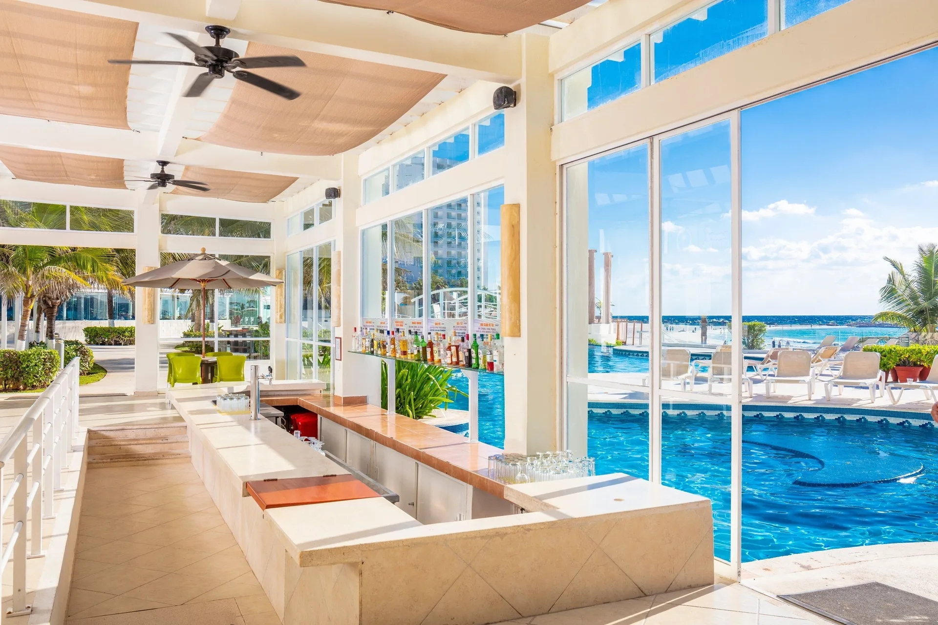 Poolside bar with glass walls, liquor bottles, and ocean views at Krystal Cancun.