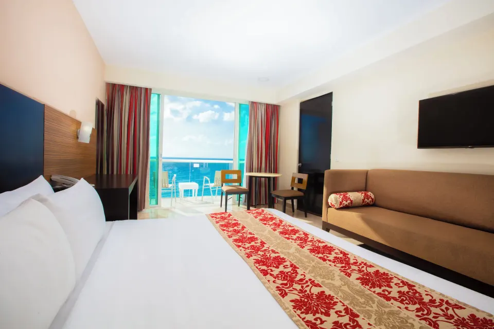 Club Room bed with sofa, balcony seating, and ocean view at Krystal Cancun.