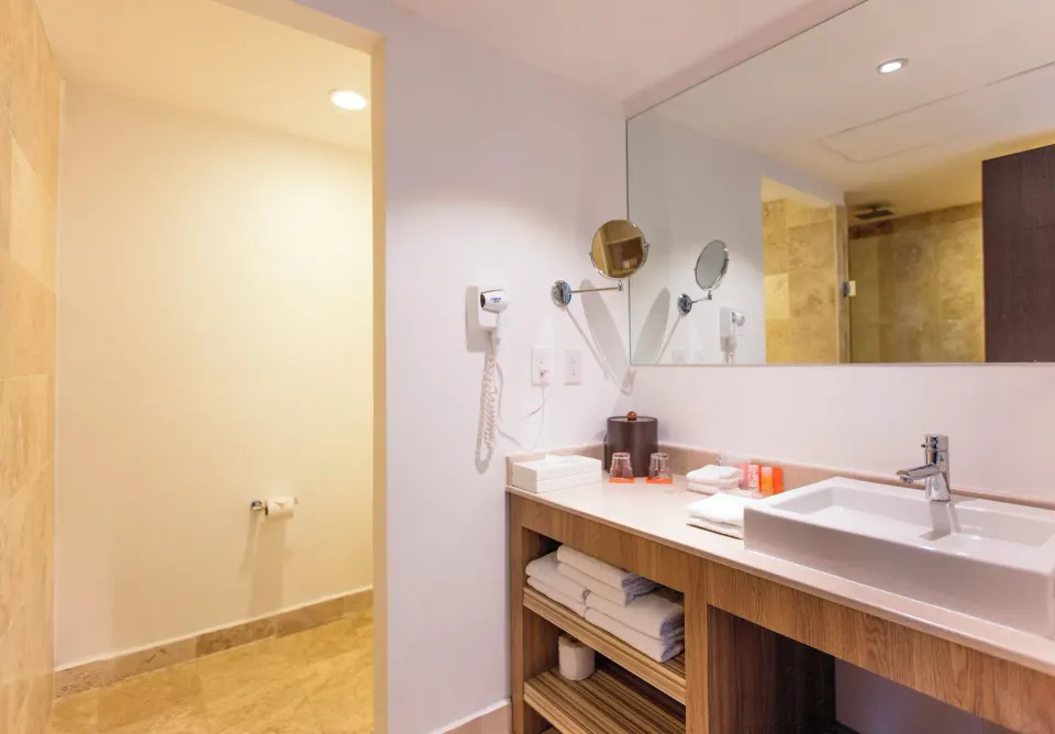 Family Studio bathroom vanity with sink, mirror, towels, and shower area at Krystal Cancun.