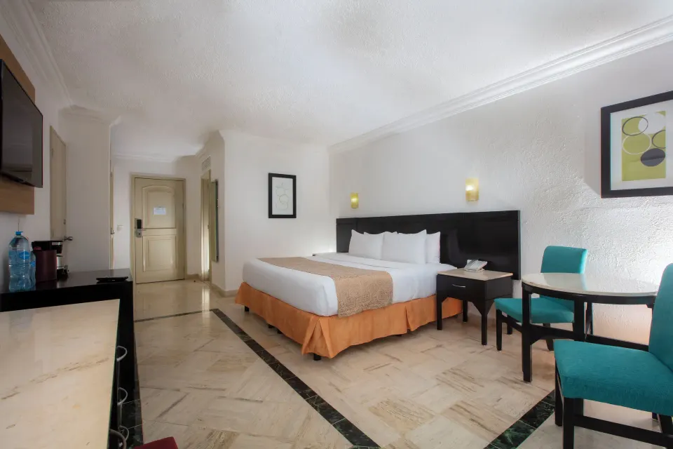 Standard Room with one bed, round table, teal chairs, and wall TV at Krystal Cancun.