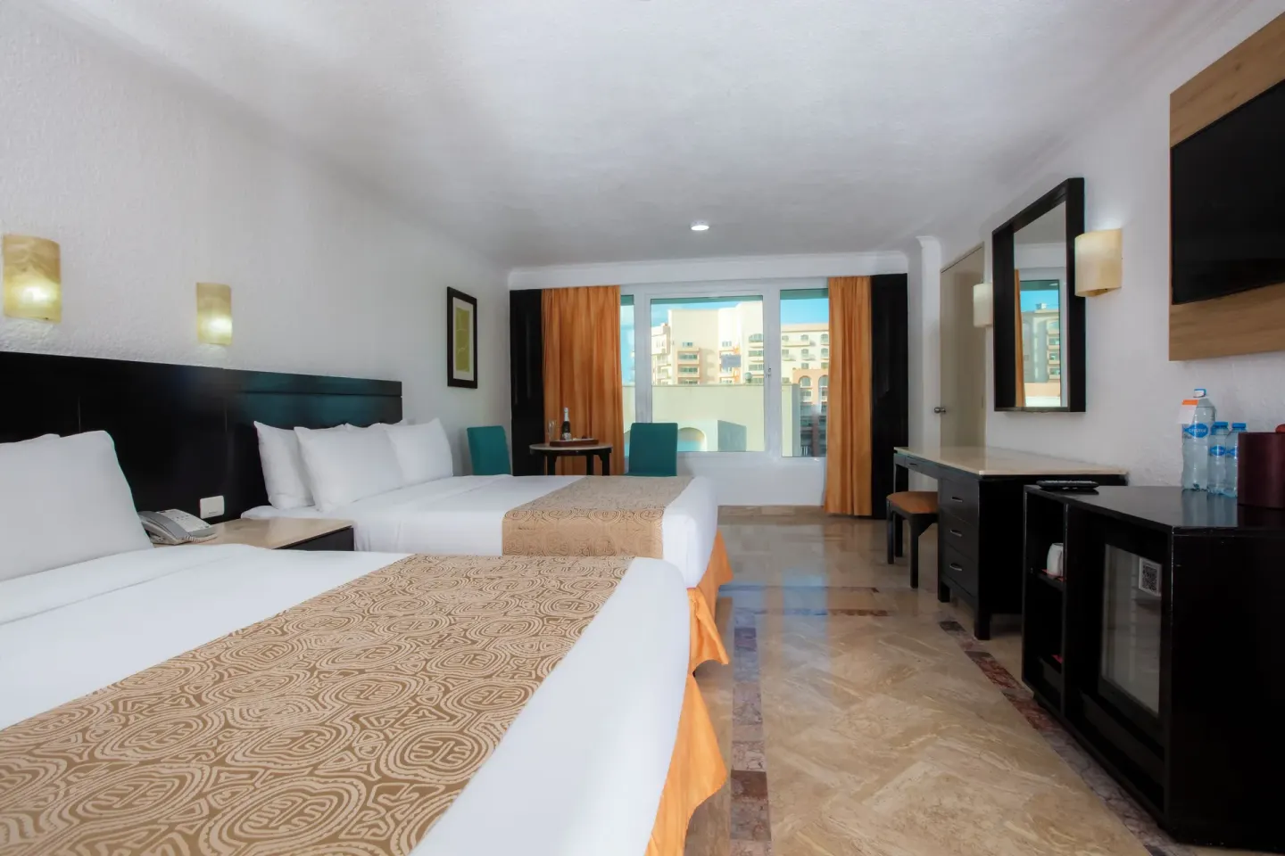 Standard Room with two beds, teal chairs, wide window, desk, TV, and mini fridge at Krystal Cancun.