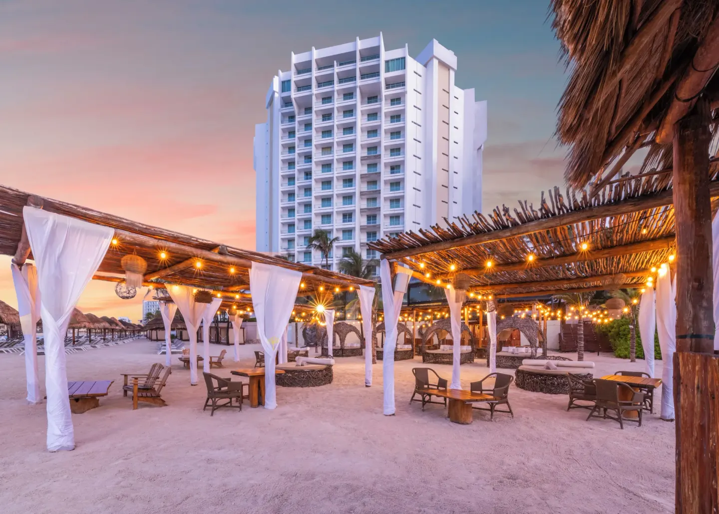 Beach lounge area with pergolas, string lights, and resort tower at Krystal Grand Cancun.