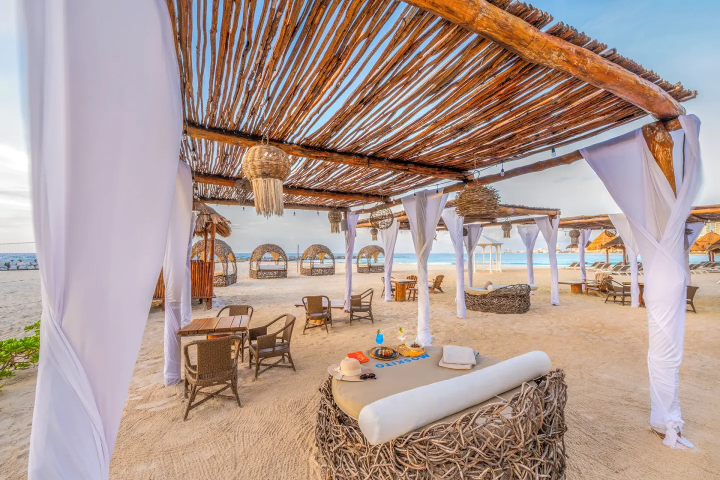 Canopied beach daybed with woven furniture and ocean views at Krystal Grand Cancun.