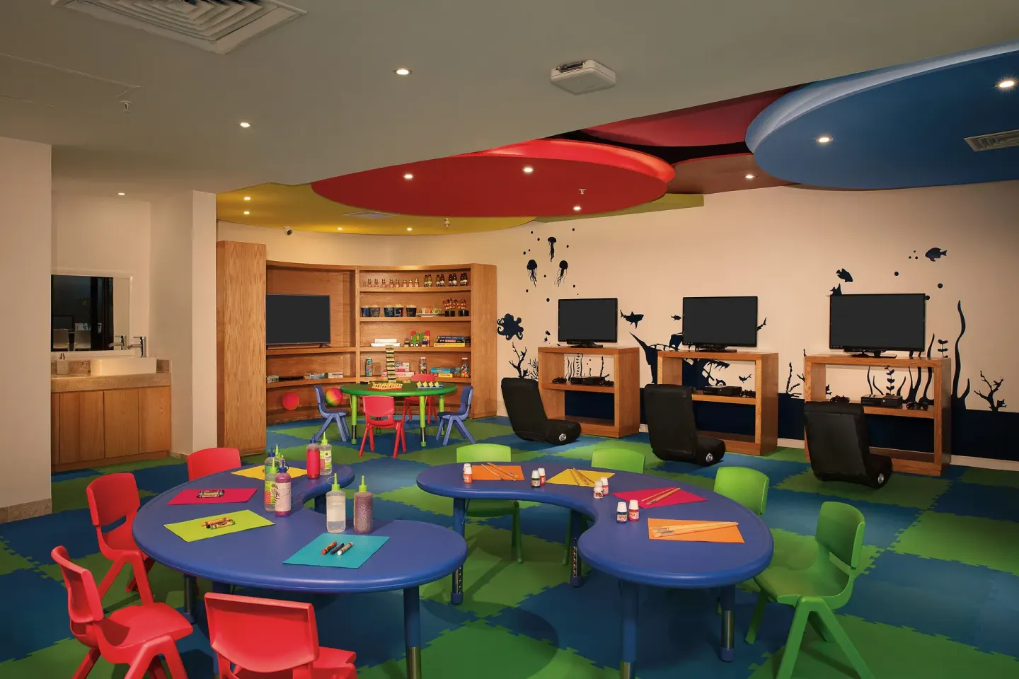 Colorful kids club with tables, chairs and screens at Krystal Grand Cancun.