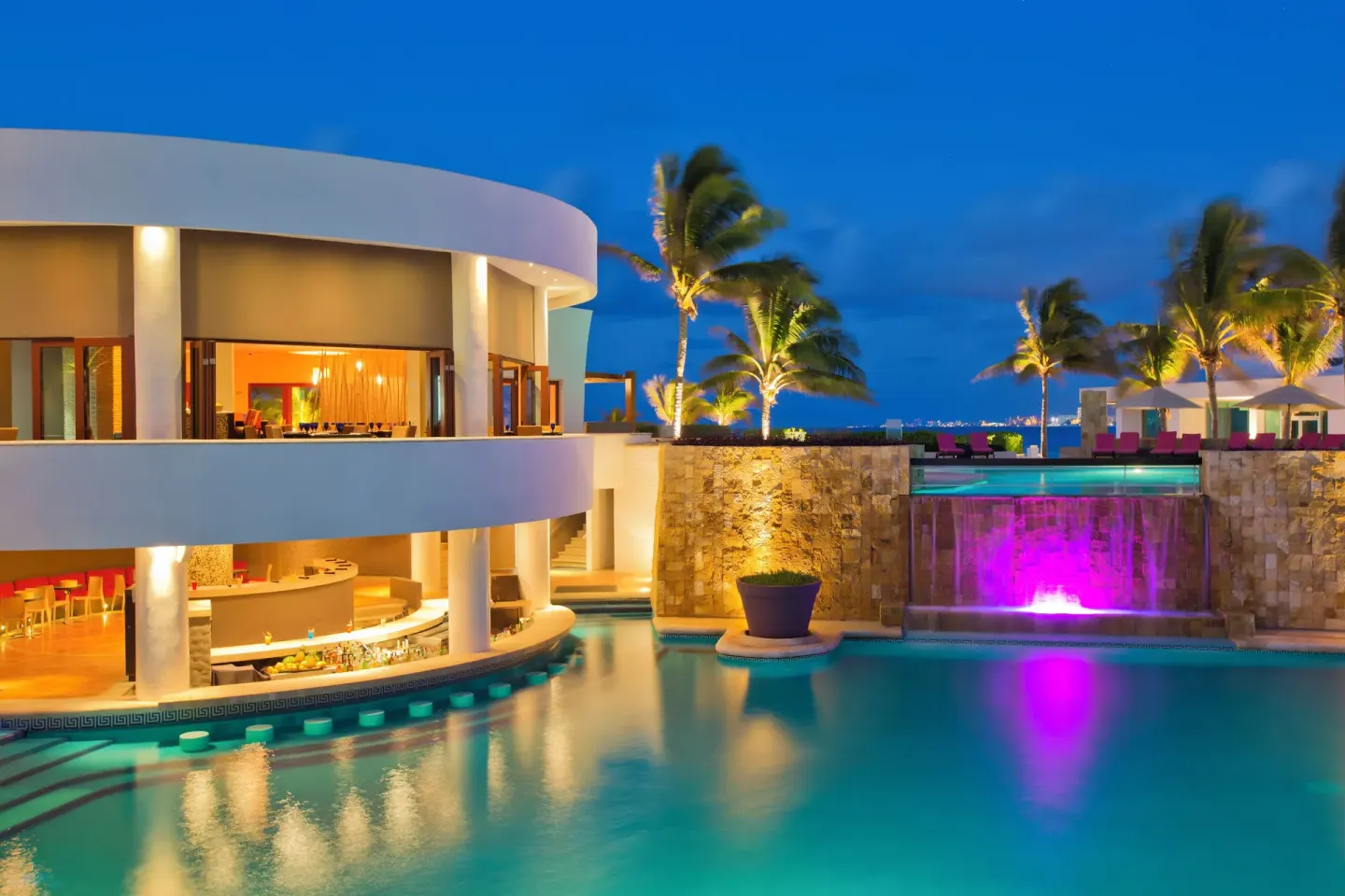 Evening pool area with lit palms and waterfall at Krystal Grand Cancun.