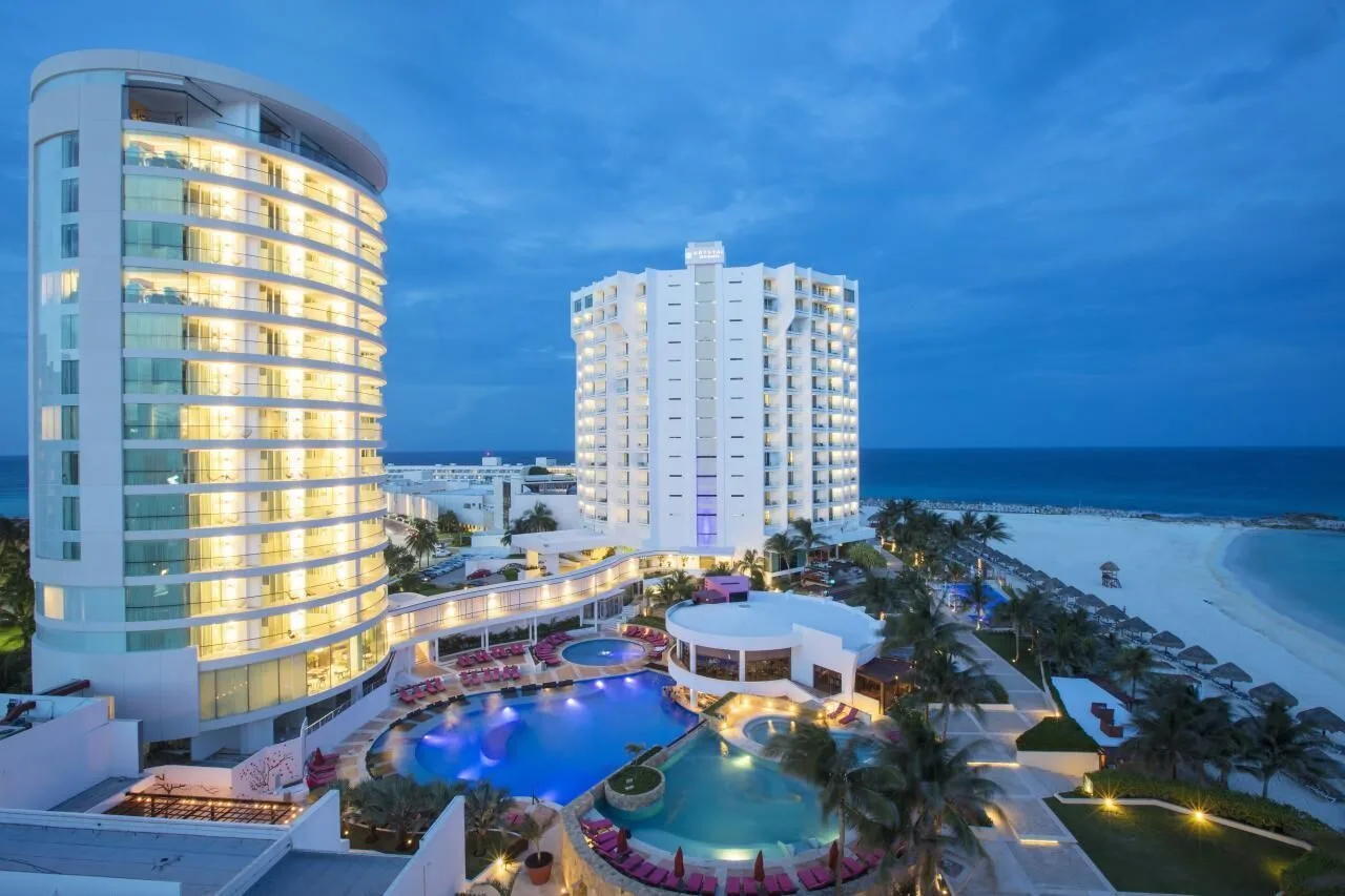 Illuminated resort towers, pools, and beach at dusk at Krystal Grand Cancun.