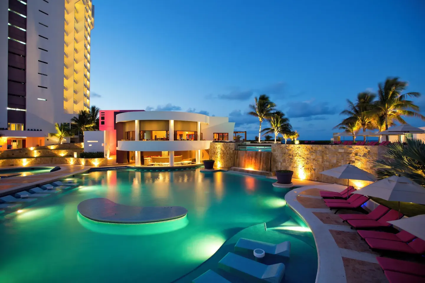 Resort pool glowing at twilight with loungers and palms at Krystal Grand Cancun.