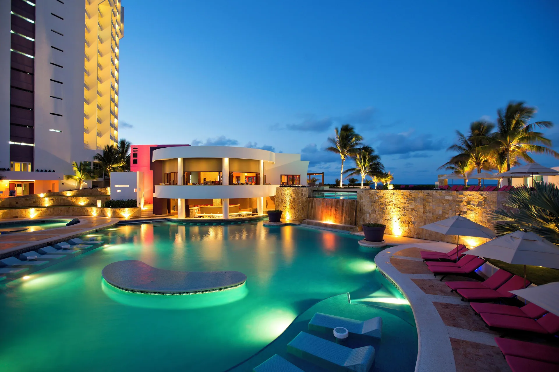 Resort pool glowing at twilight with loungers and palms at Krystal Grand Cancun.