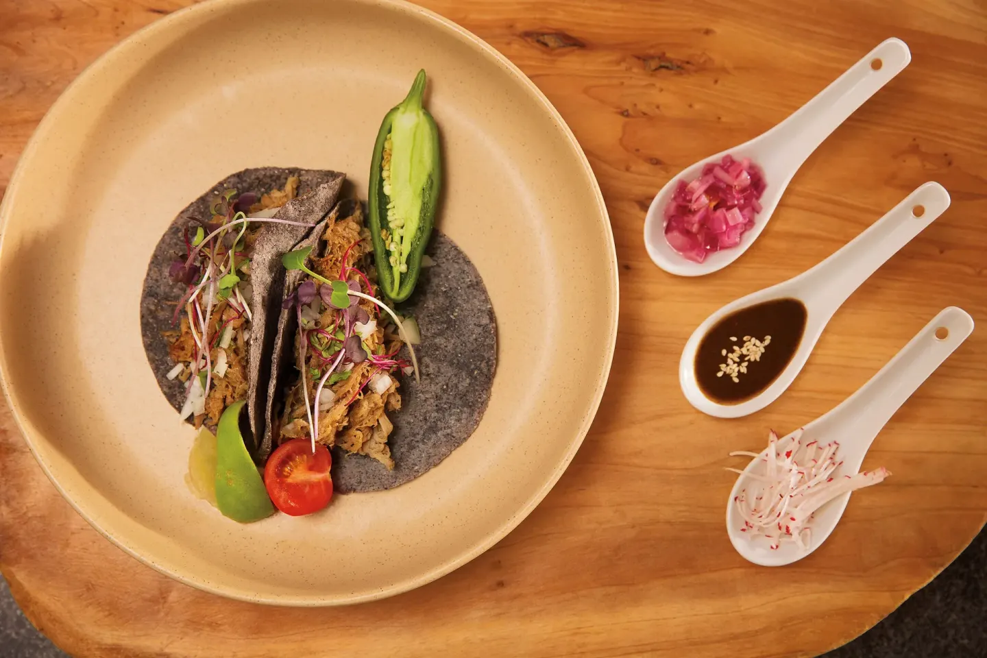 Plated tacos with garnishes and sauces on a wooden table at Krystal Grand Cancun.