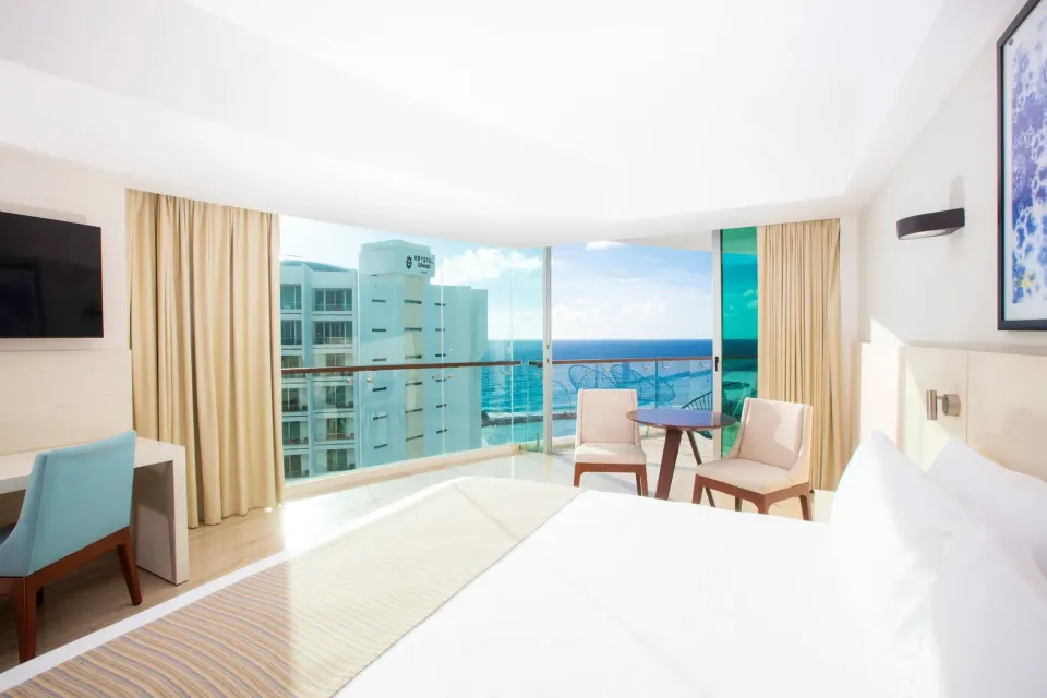Altitude Corner Suite bed, desk, and ocean-facing sitting area at Krystal Grand Cancun.