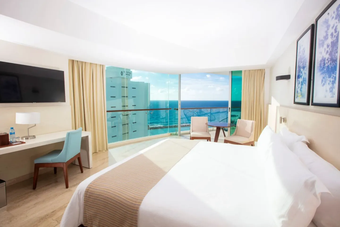 King bed, desk, balcony seating, and partial ocean view in a suite at Krystal Grand Cancun.
