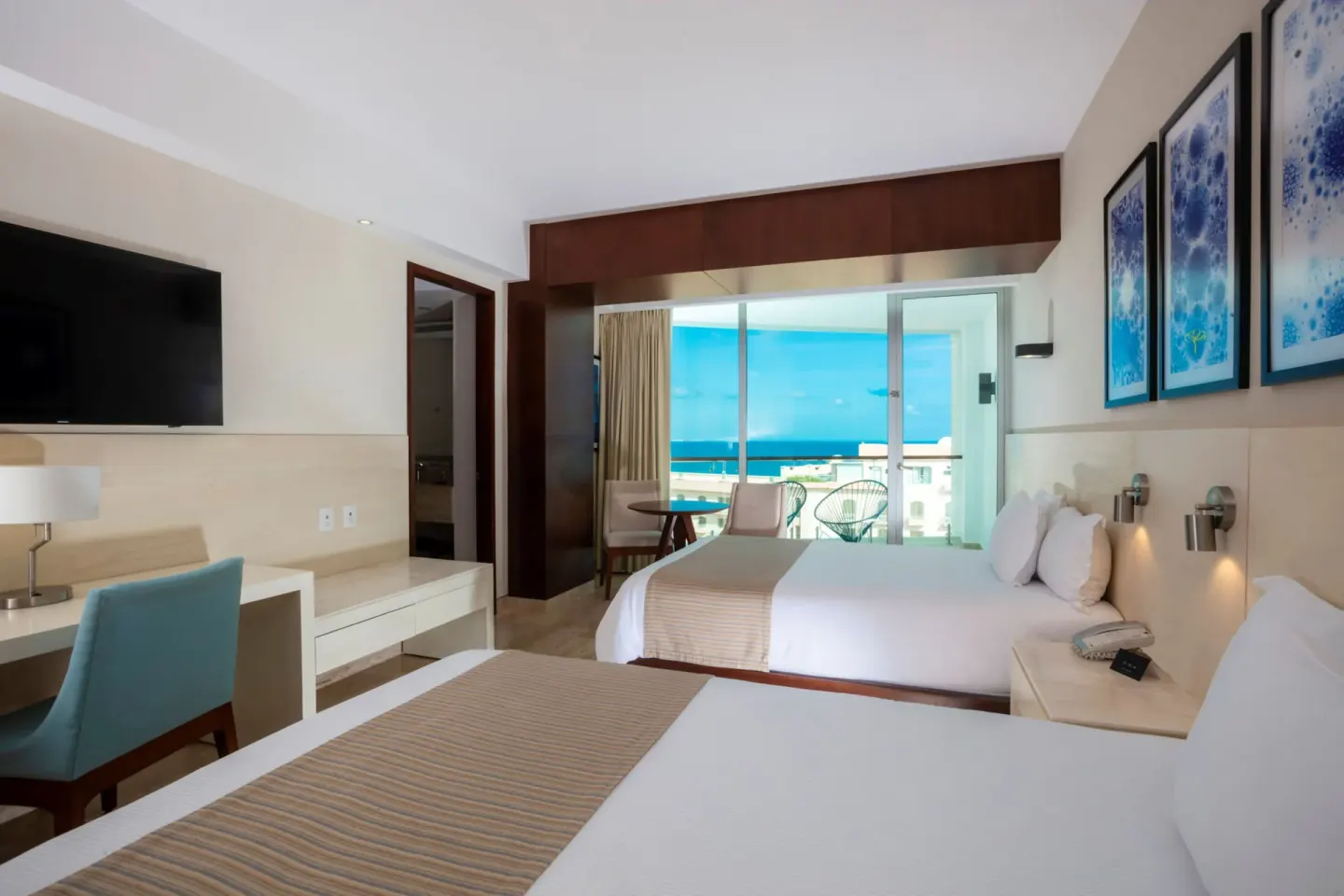 Two double beds with balcony doors and ocean beyond in an Altitude Suite at Krystal Grand Cancun.