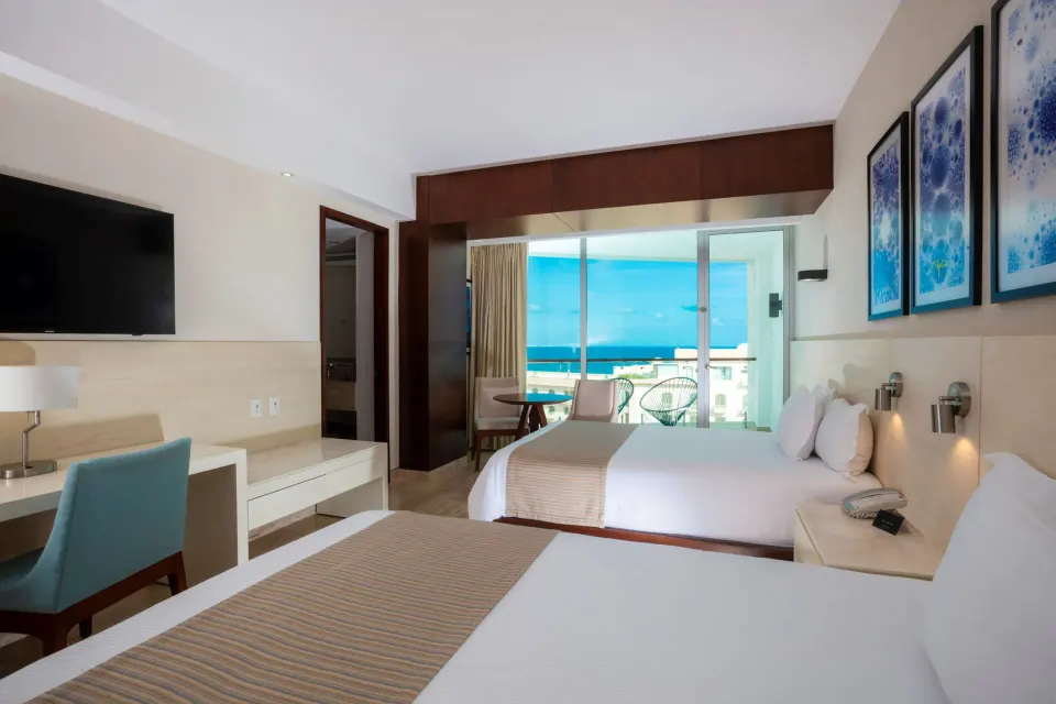 Two double beds with balcony doors and ocean beyond in an Altitude Suite at Krystal Grand Cancun.