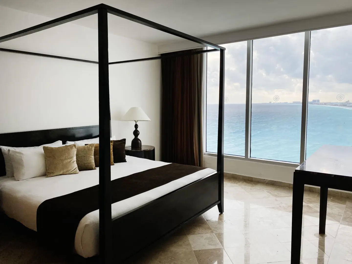 Presidential Room Ocean View king bed by large sea-facing windows at Krystal Grand Cancun.