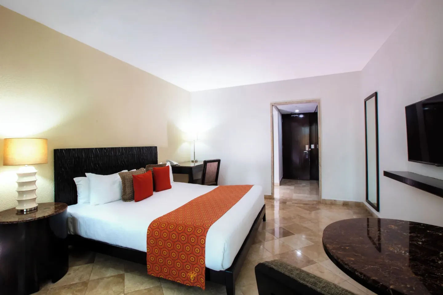Standard Room king bed with orange bed runner at Krystal Grand Cancun.