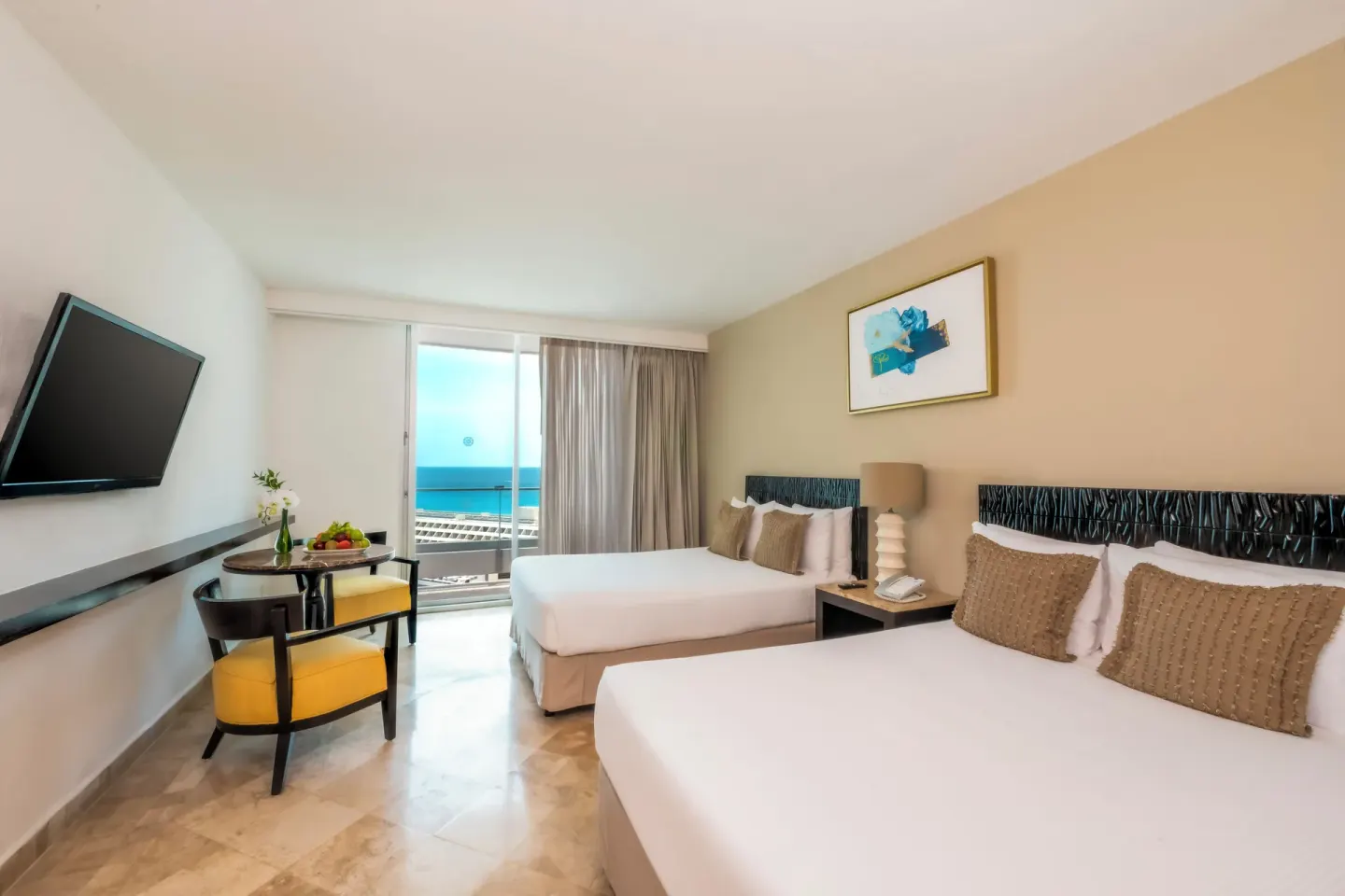 Standard Room with two beds, table, TV, and ocean view balcony at Krystal Grand Cancun.