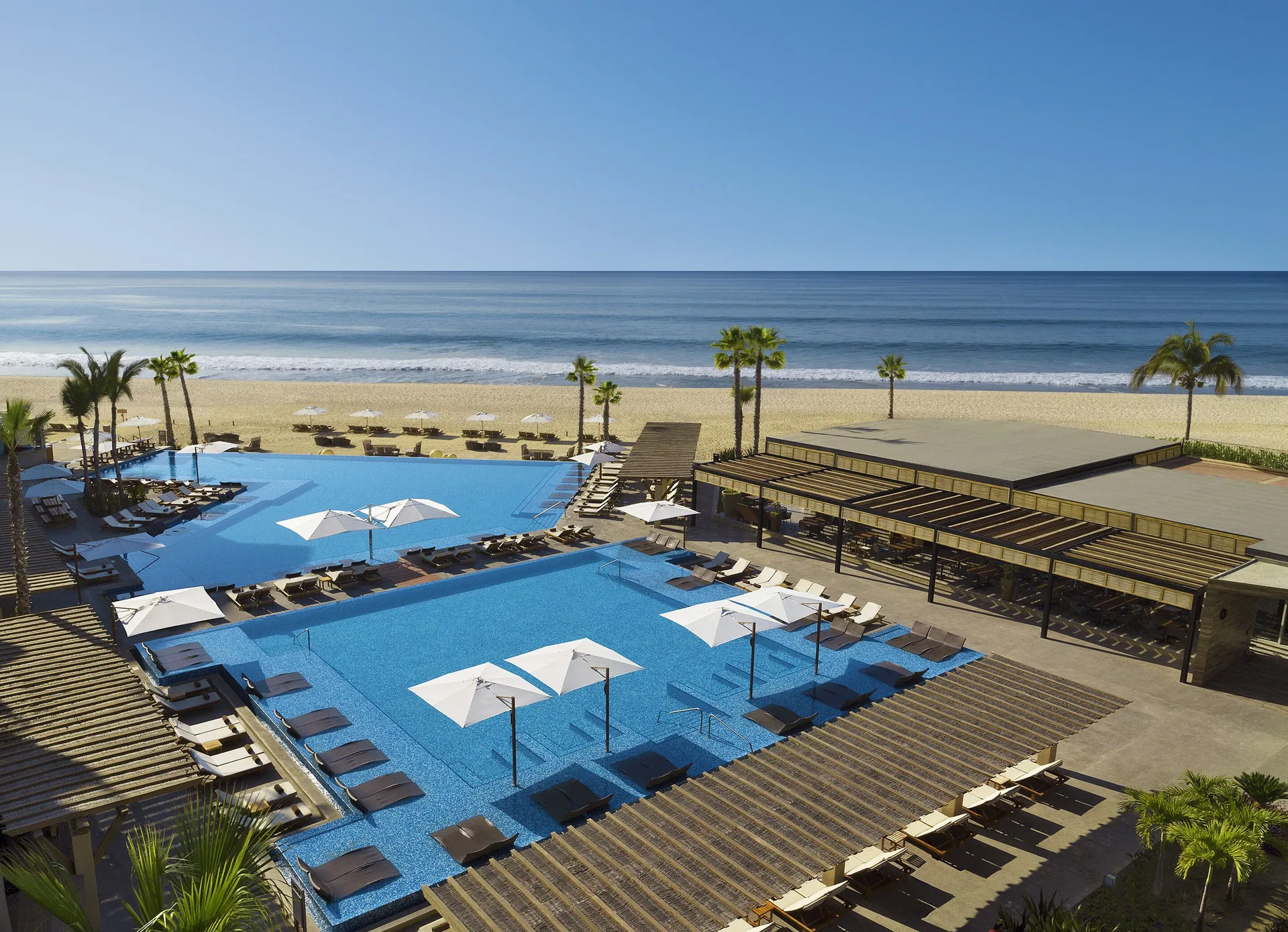 Beachfront pools, loungers, palm trees and ocean at Krystal Grand Los Cabos.