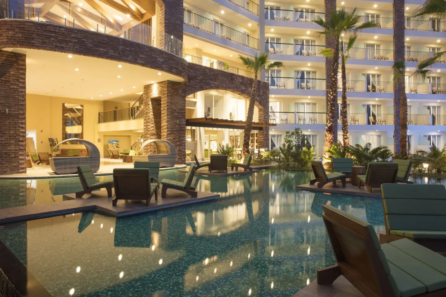 Evening pool with lounge chairs and lit guestroom balconies at Krystal Grand Los Cabos.