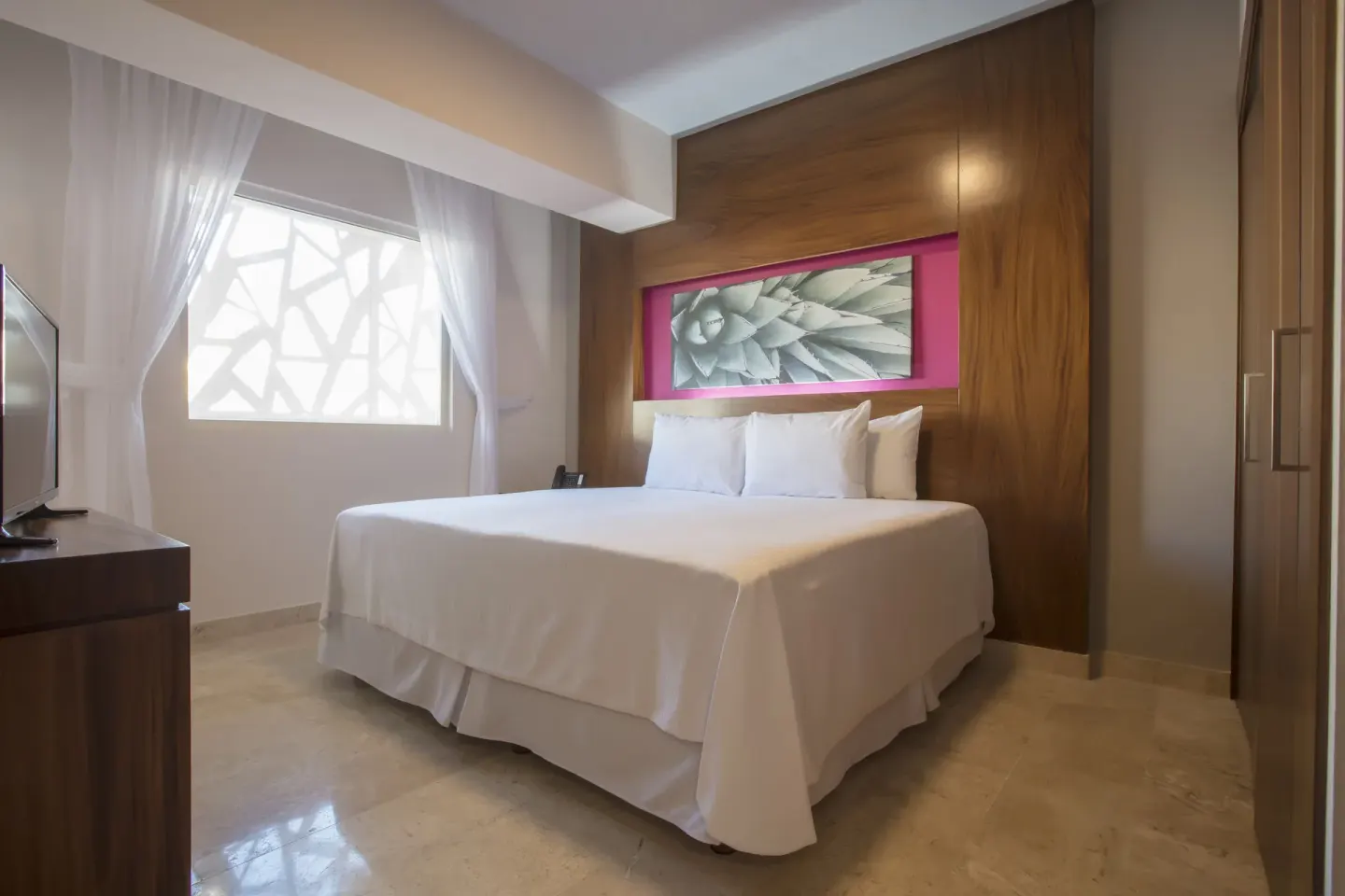 Guest room with king bed, wood headboard and patterned window at Krystal Grand Los Cabos.