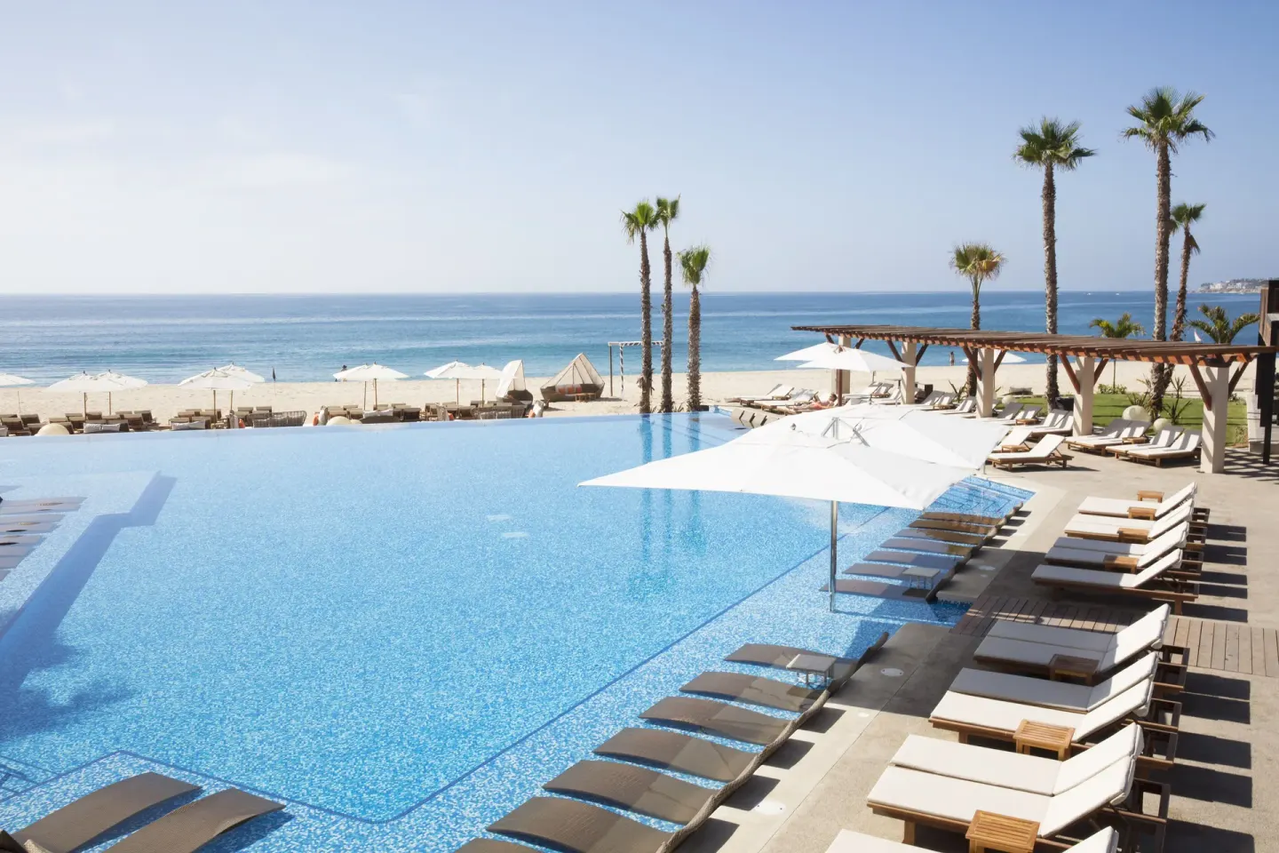 Infinity pool with white umbrellas by the beach at Krystal Grand Los Cabos.