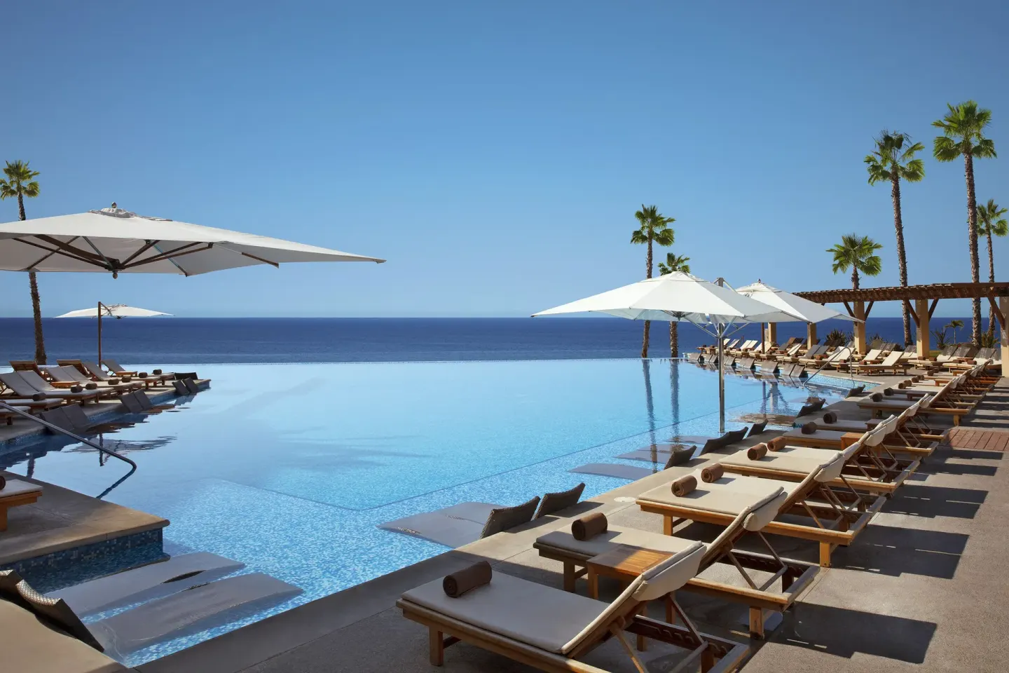 Infinity pool with loungers and white umbrellas at Krystal Grand Los Cabos.