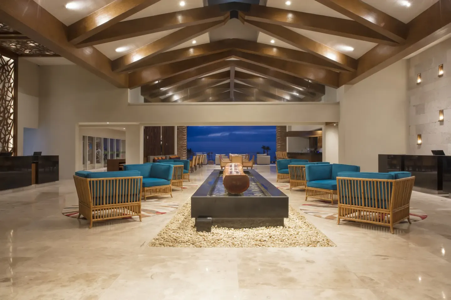 Lobby seating with wood beams, teal chairs and ocean beyond at Krystal Grand Los Cabos.