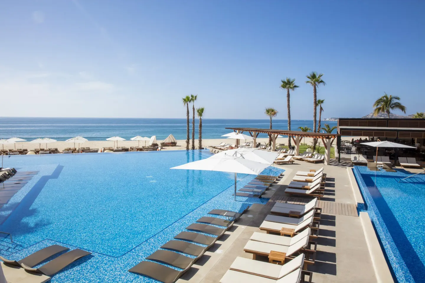 Oceanfront infinity pool deck with loungers at Krystal Grand Los Cabos.
