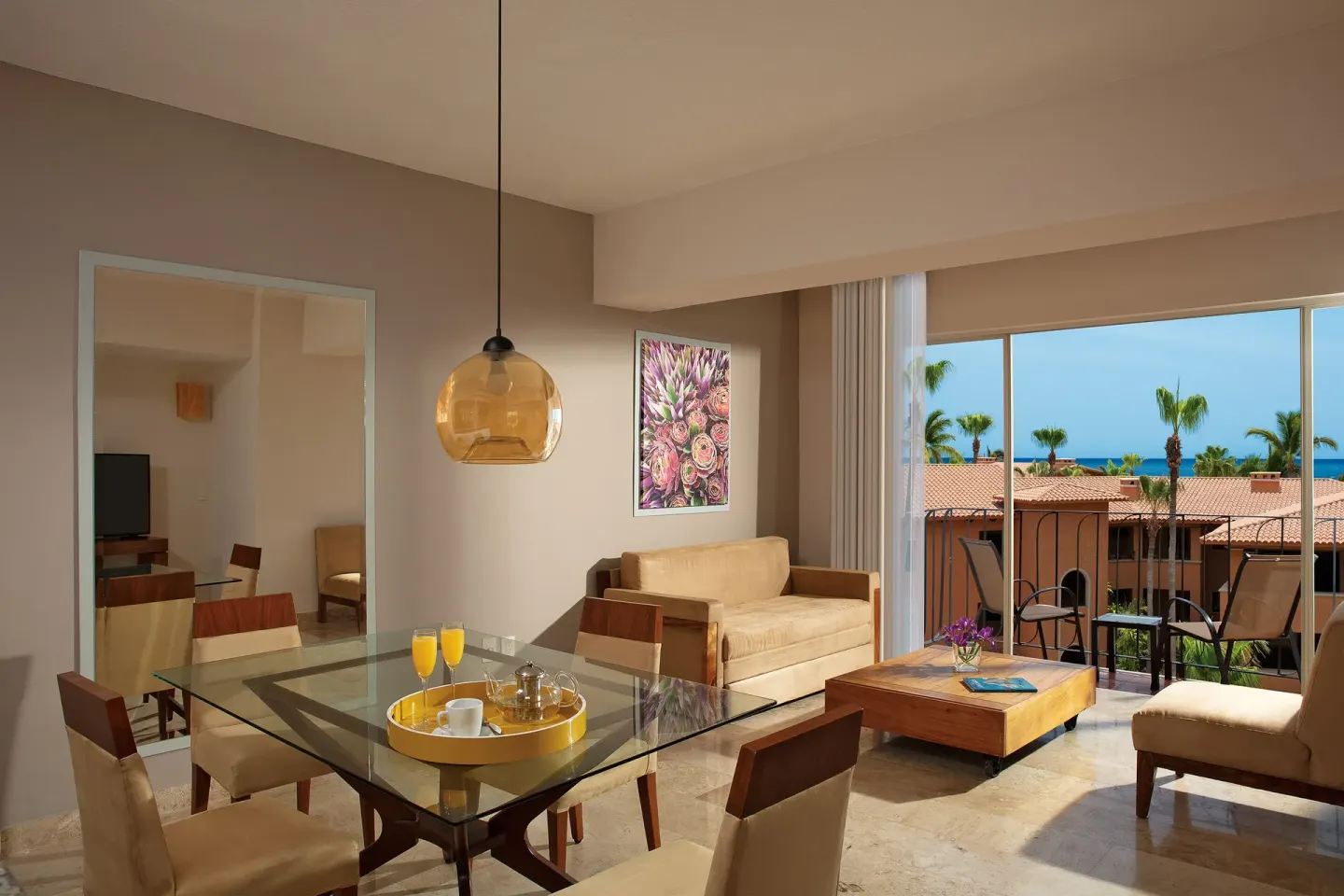 Suite living room with glass dining table and balcony at Krystal Grand Los Cabos.