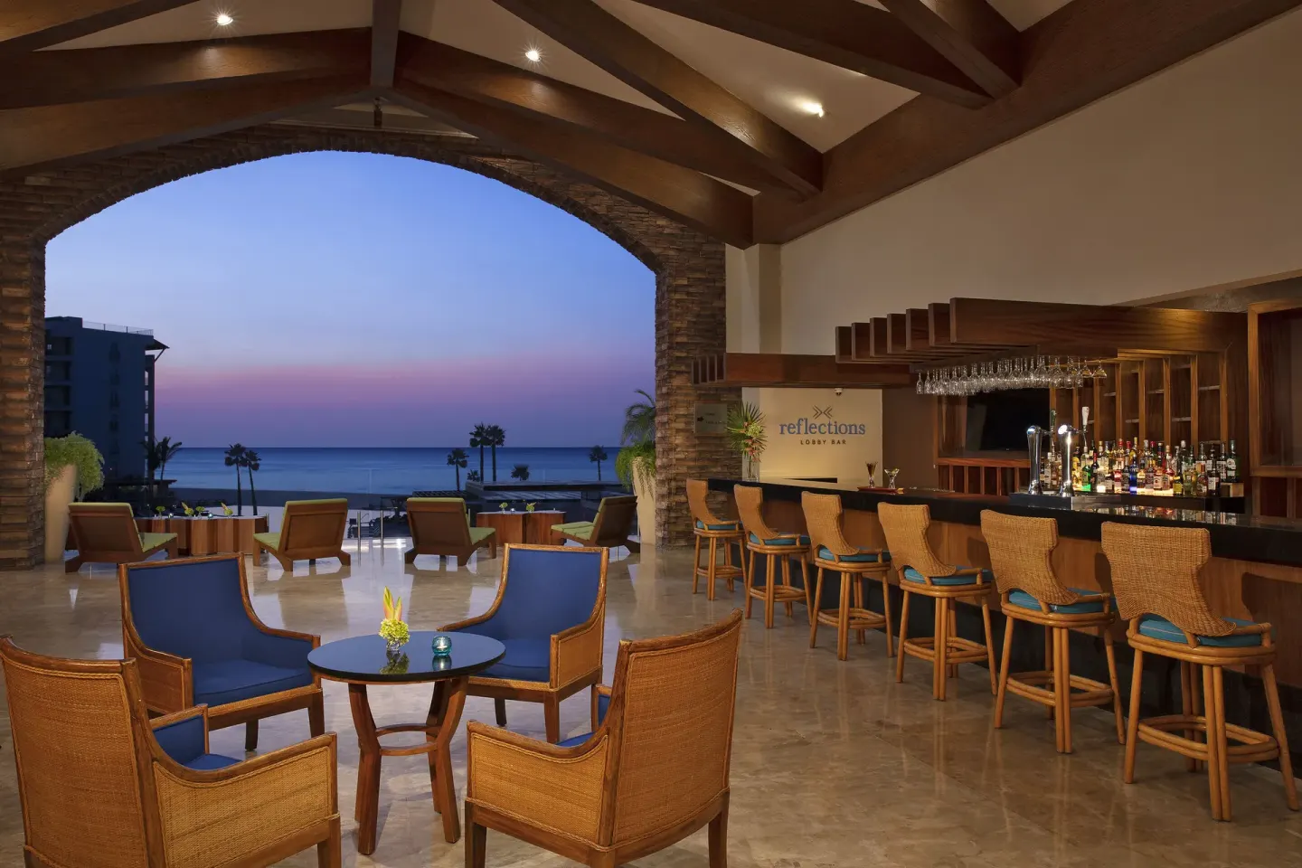 Lobby bar with wicker stools, lounge seating and sunset ocean view at Krystal Grand Los Cabos.