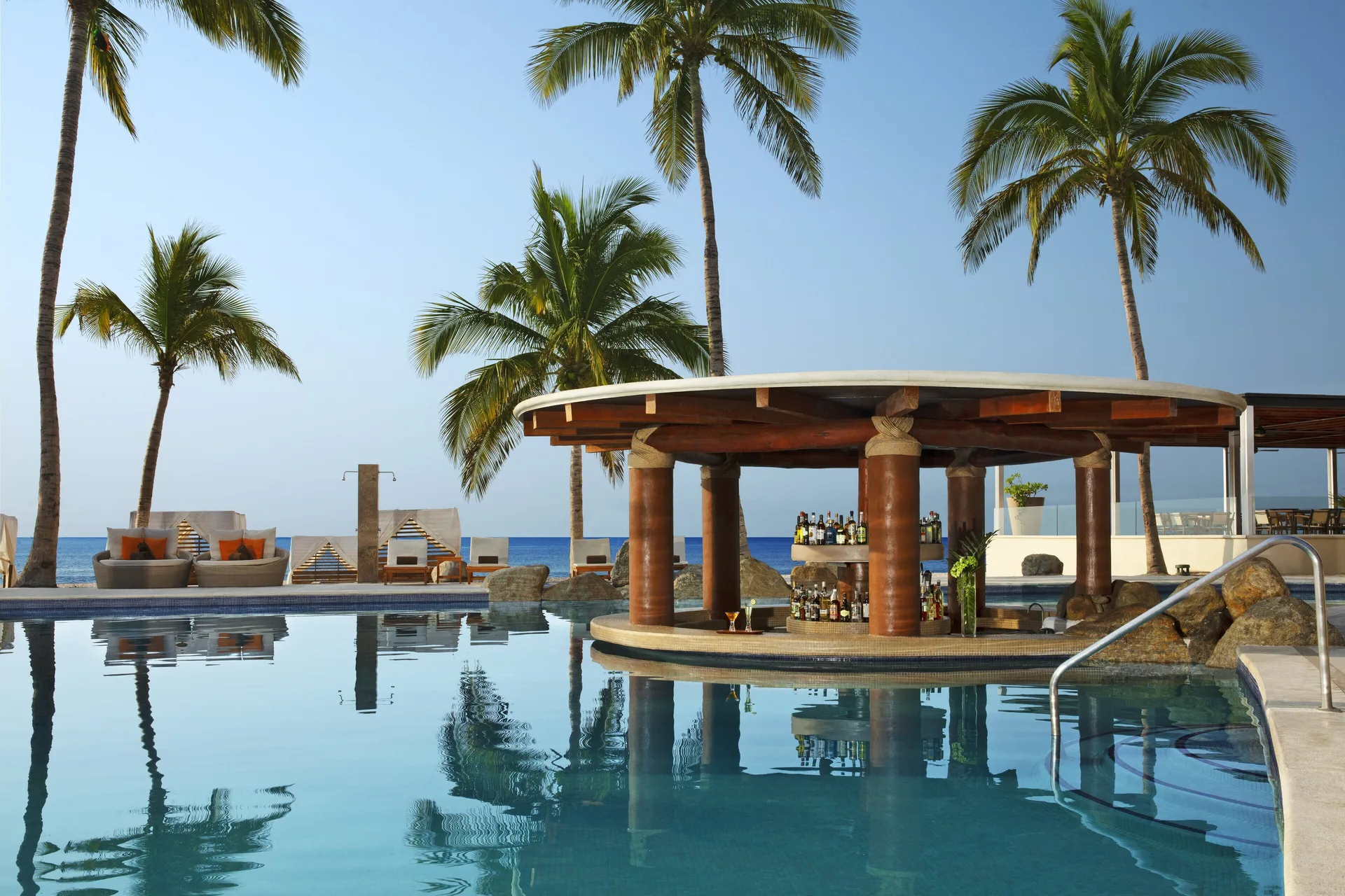 Swim-up pool bar with palm trees and ocean beyond at Krystal Grand Los Cabos.