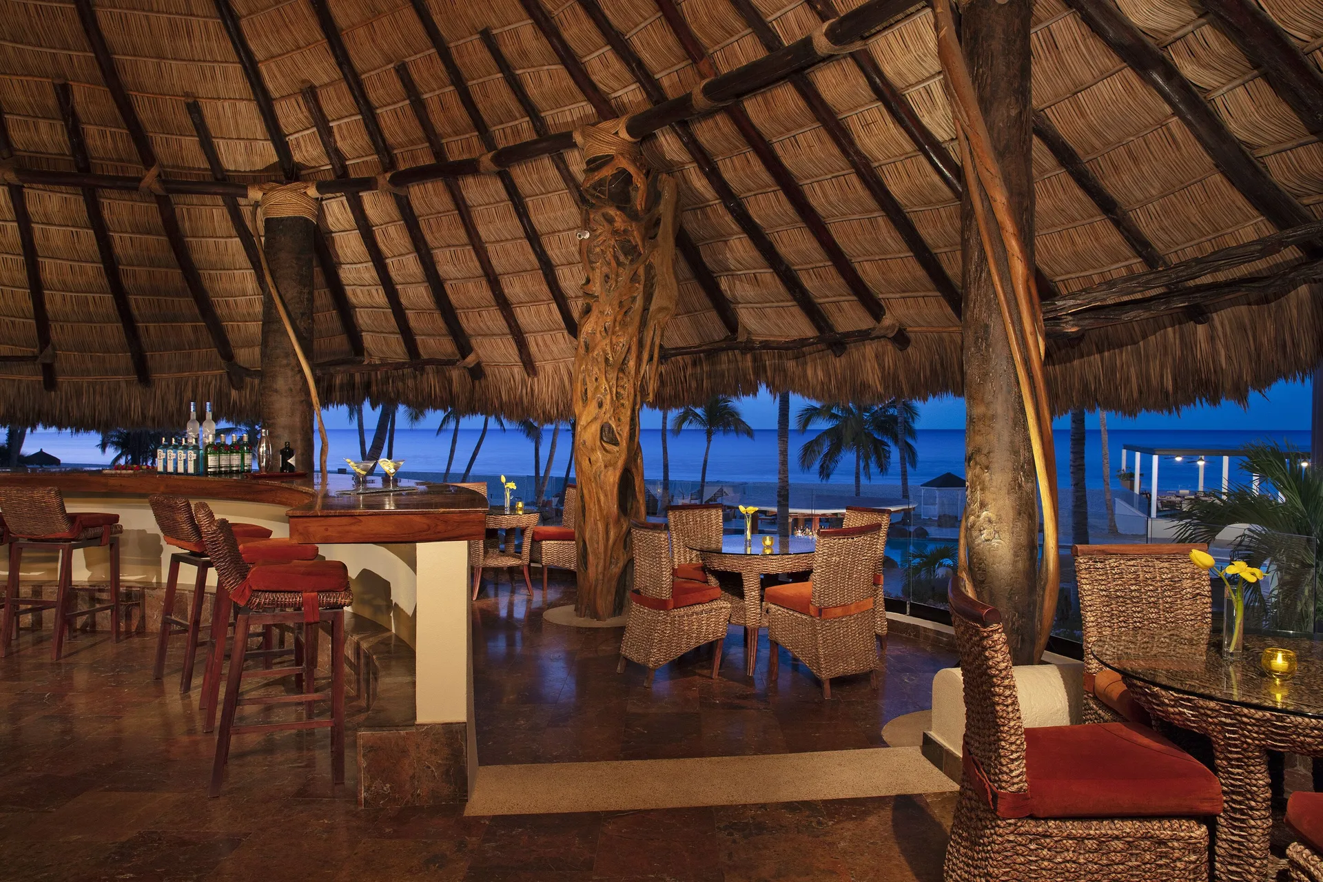 Thatched-roof bar with wicker seating and ocean views at Krystal Grand Los Cabos.