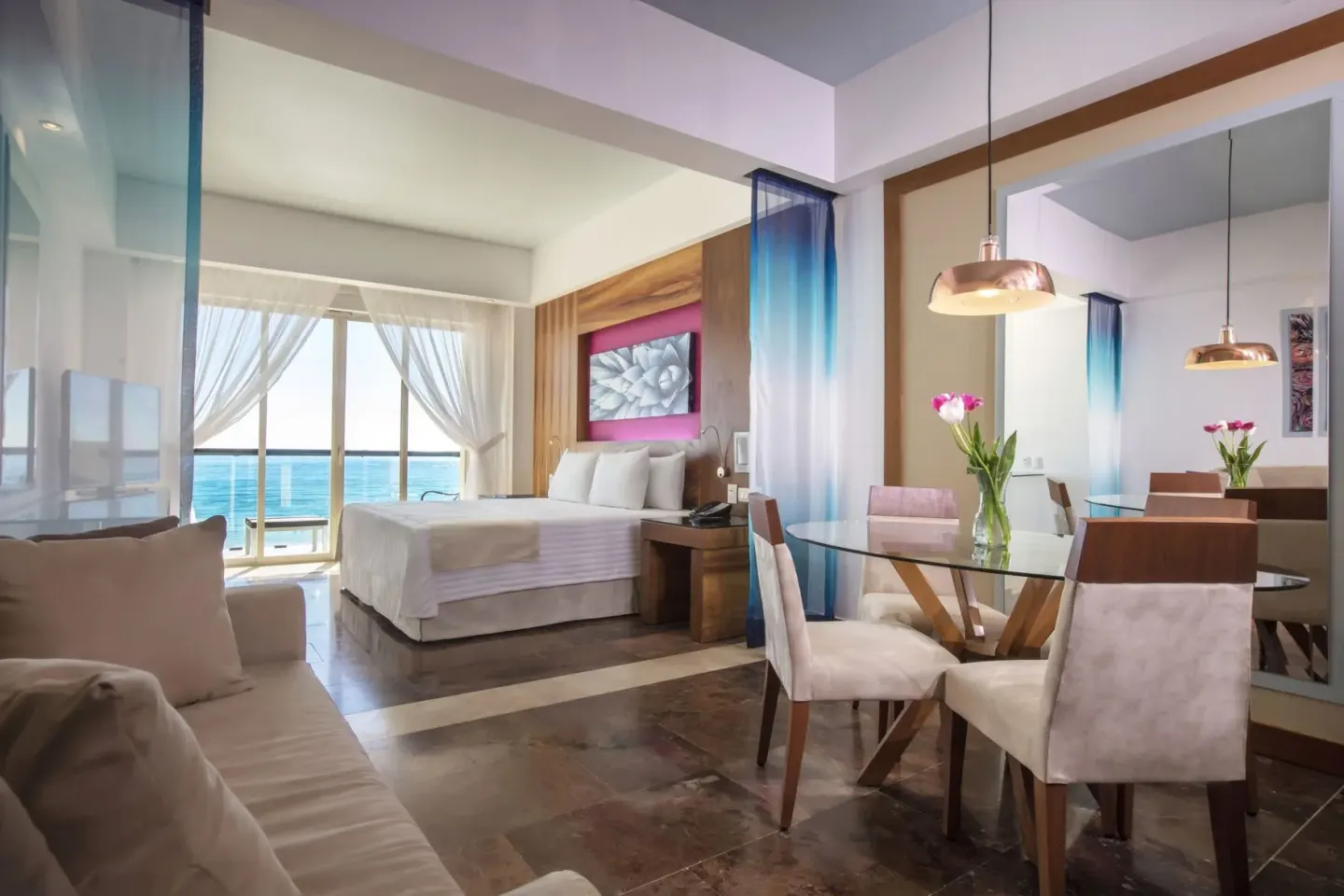 Oceanfront junior suite with bed, sofa, dining table and balcony at Krystal Grand Los Cabos.