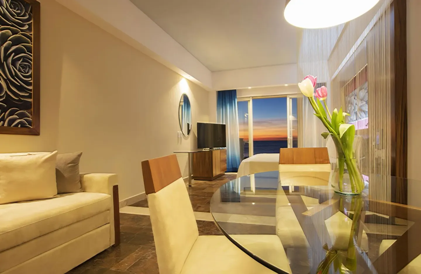 Junior suite sitting area with glass dining table and ocean sunset view at Krystal Grand Los Cabos.