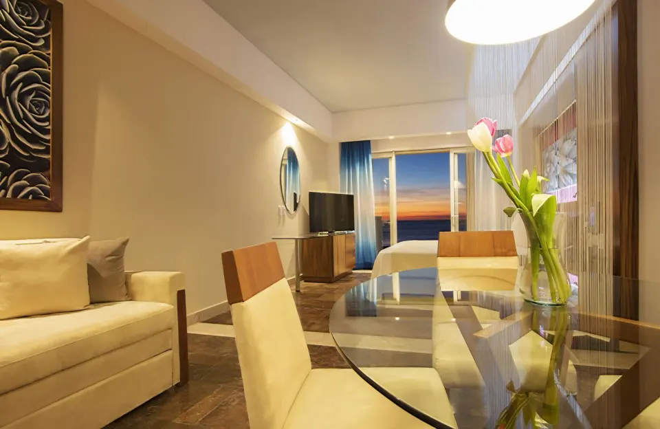 Junior suite sitting area with glass dining table and ocean sunset view at Krystal Grand Los Cabos.