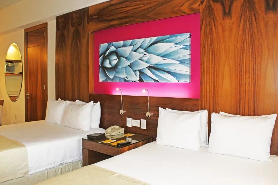 Two beds with white linens and a wood headboard wall at Krystal Grand Los Cabos.