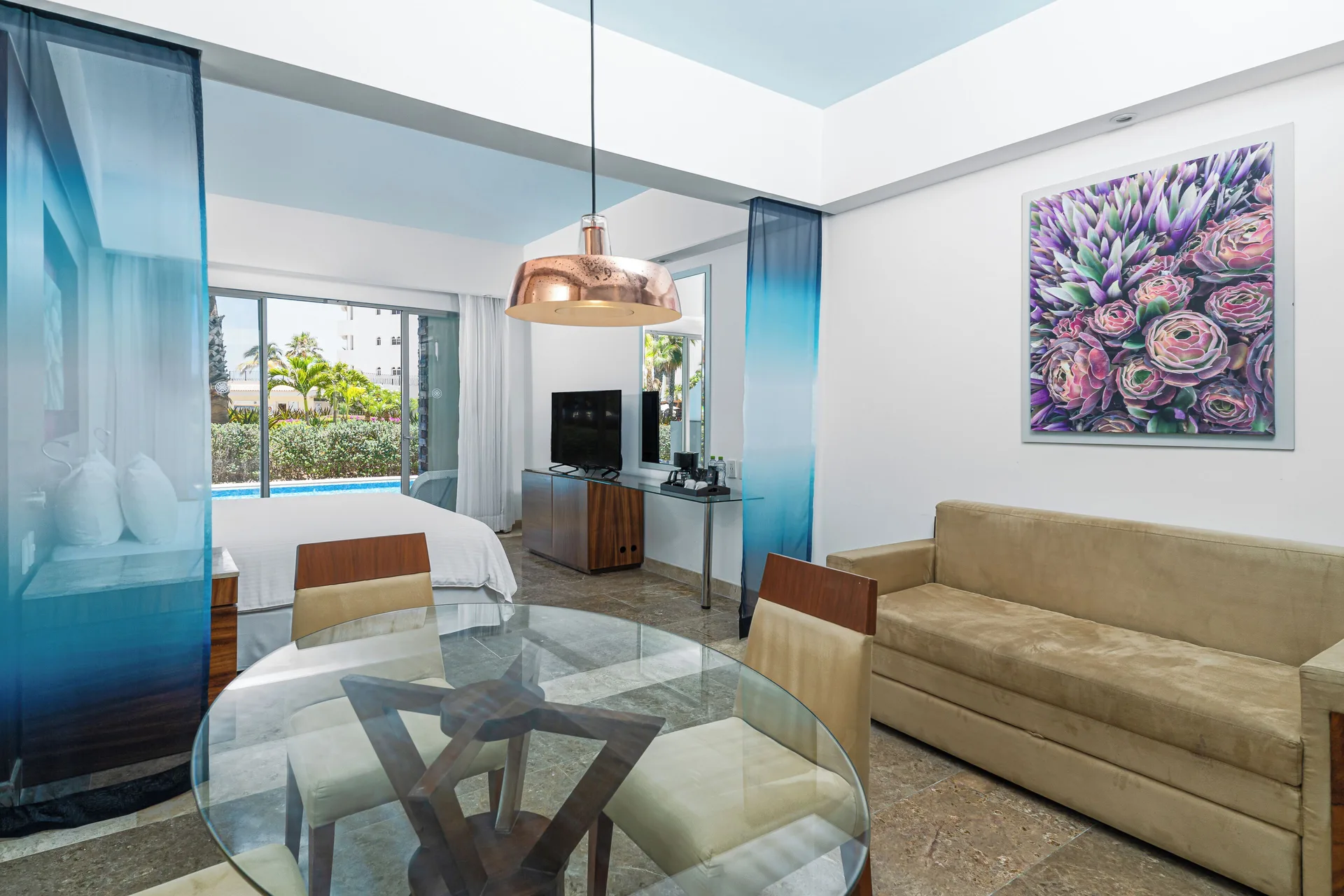 Altitude Junior Suite swimout garden view living area at Krystal Grand Los Cabos with sofa, dining table, and bed.