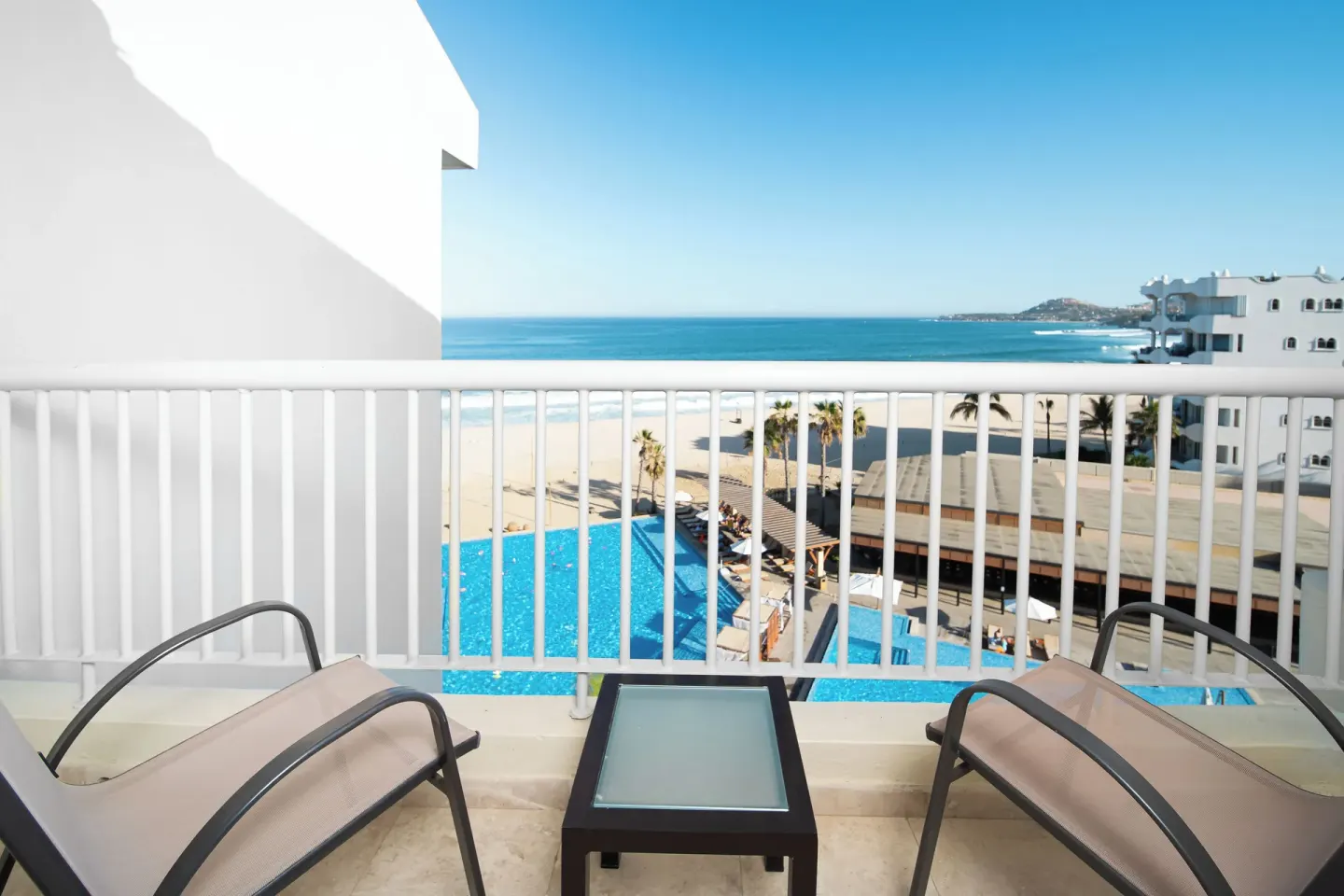 Suite Palmilla Ocean View balcony with two chairs and pool below at Krystal Grand Los Cabos.
