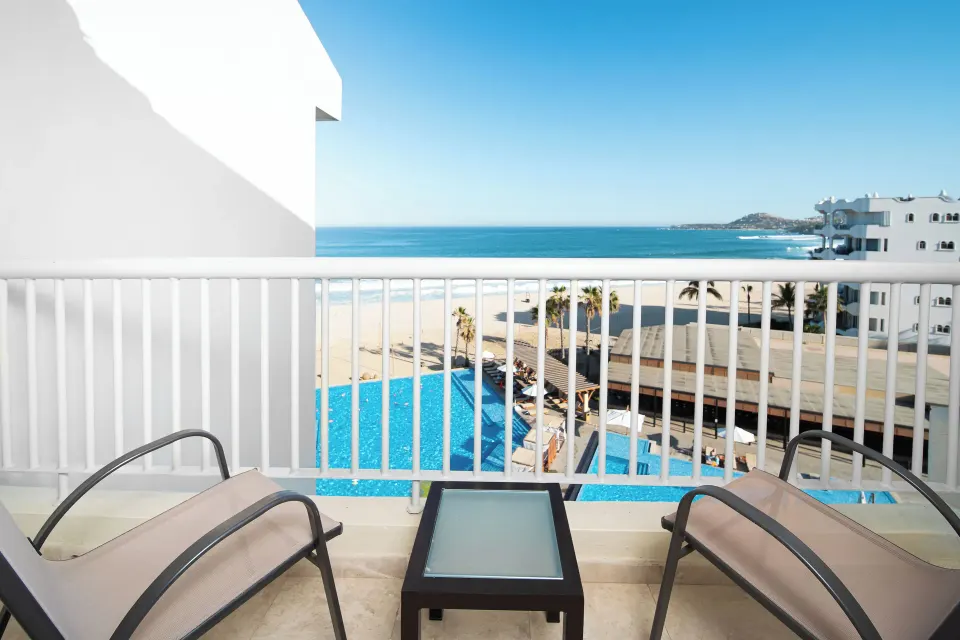 Suite Palmilla Ocean View balcony with two chairs and pool below at Krystal Grand Los Cabos.