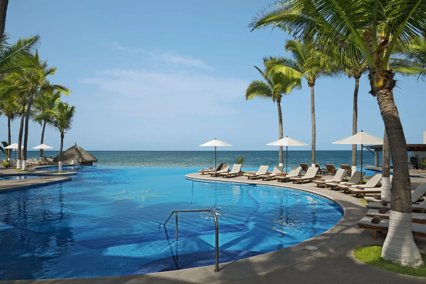 Oceanfront swimming pool with loungers and palms at Krystal Grand Nuevo Vallarta.