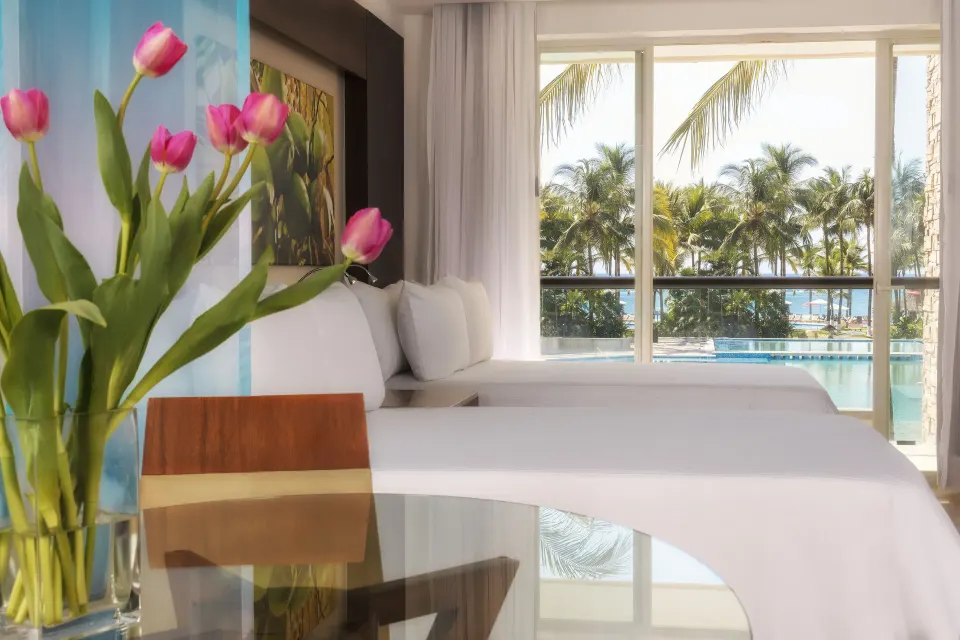 Junior Suite Pool View Doble with two beds, flowers, and pool view at Krystal Grand Nuevo Vallarta.