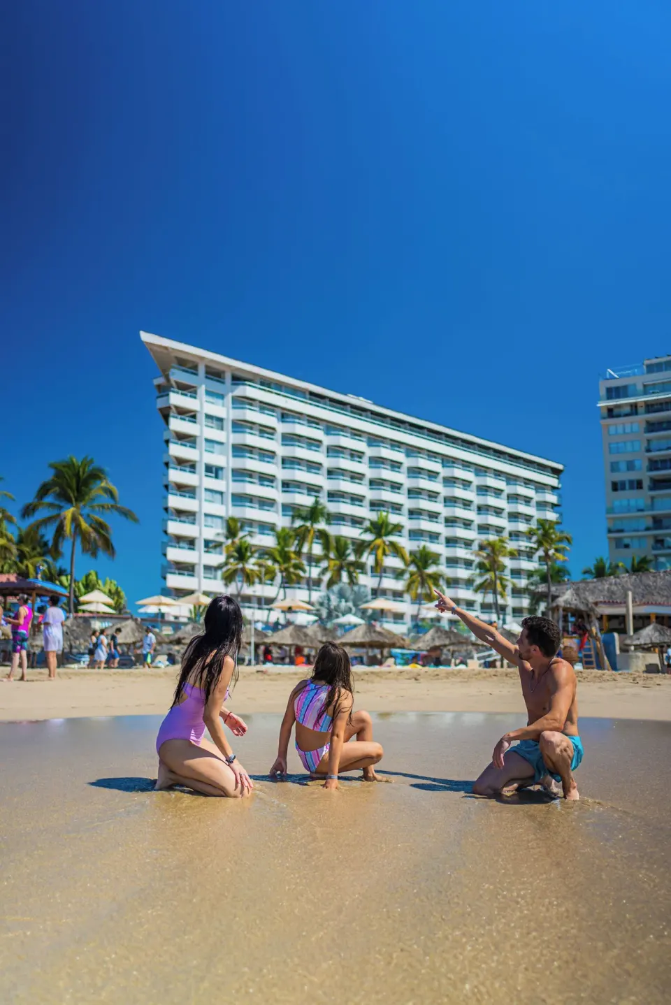 Family sitting at the shoreline with hotel tower behind them at Krystal Ixtapa.