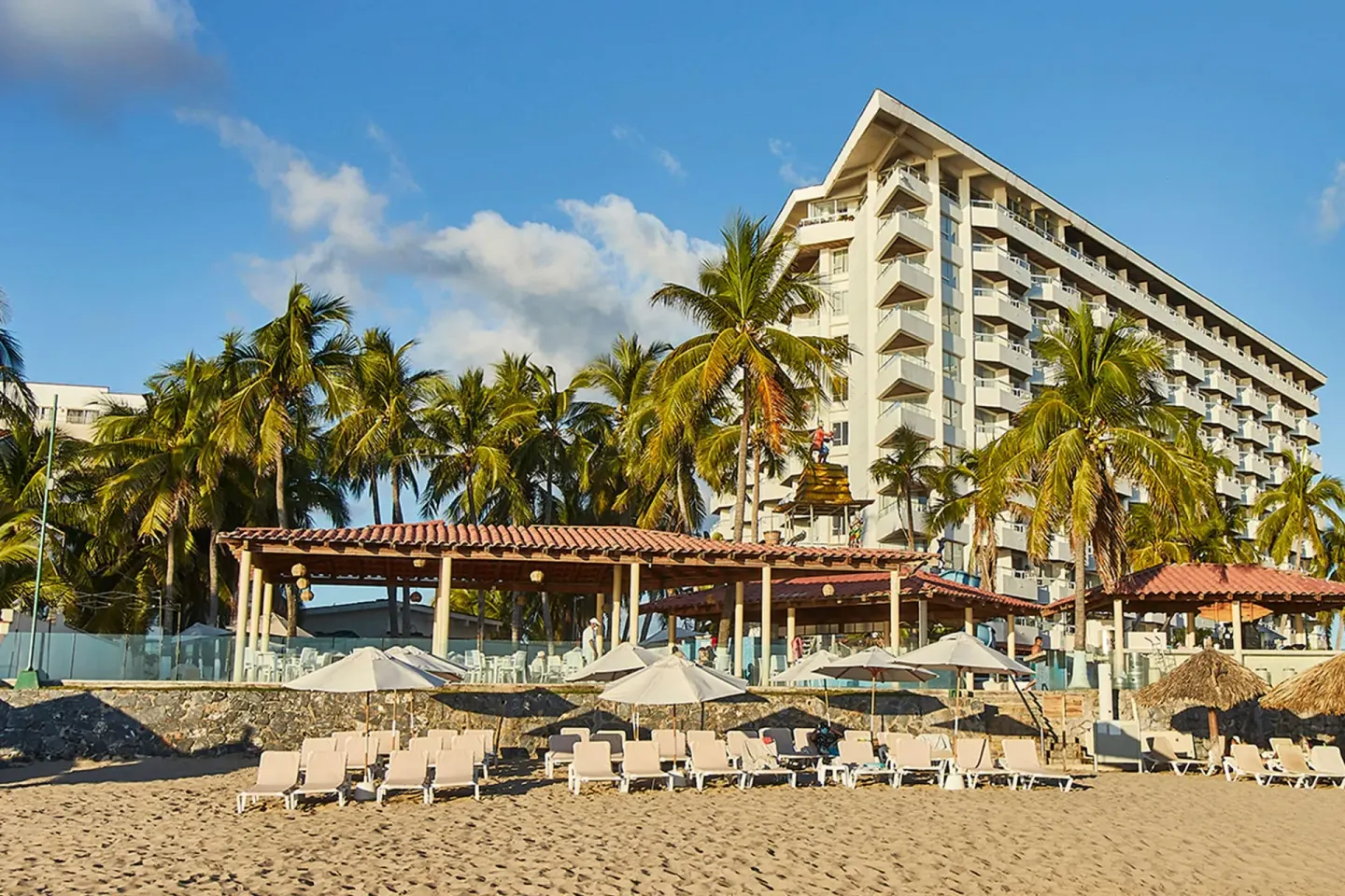 Beach loungers, palapas, palms, and tower exterior at Krystal Ixtapa.
