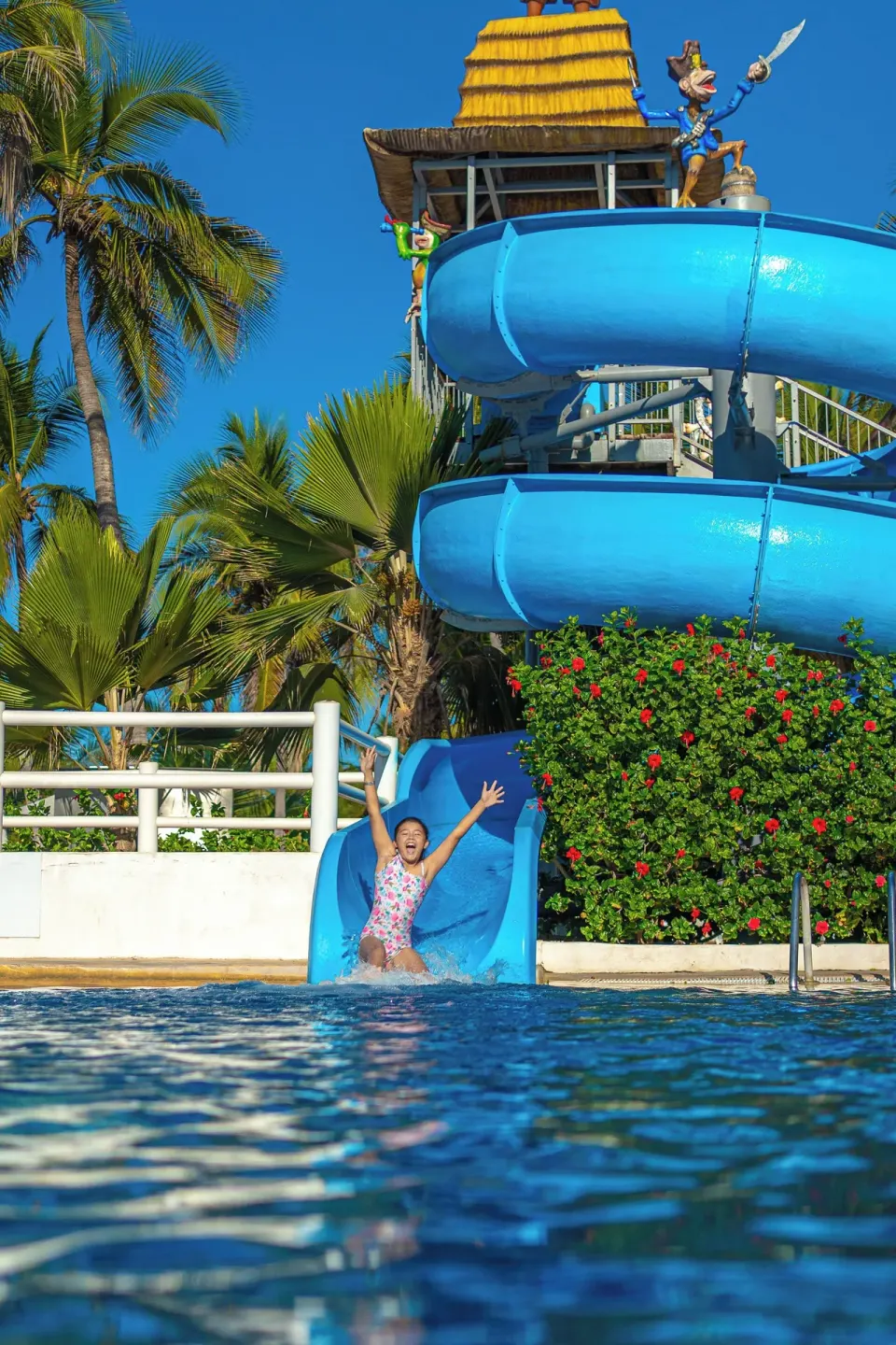 Child exiting a blue waterslide into the pool at Krystal Ixtapa.
