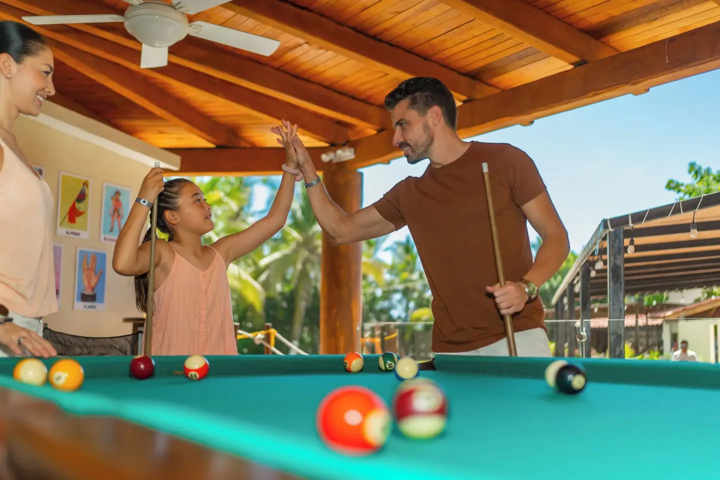 A family plays pool together in a covered recreation area at Krystal Ixtapa.